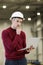 Young man, factory engineer in red pullover and white hard hat holding smartphone and laptop organizing and controlling the work