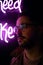 A young man fashionably dressed standing in the street at night. Illuminated signboards, neon, lights.