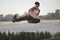 Young man fighter performs flying kick in front of skyline