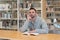 Young man with finger on his face thinking about possible answers with a book on the table in the library