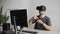 Young man finish using virtual reality goggles headset and sitting in the office against computer and trying to touch