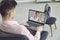 A young man freelancer sits at home in a chair and calls a doctor online. A woman doctor waves her hand to her patient.