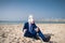 Young man in funny mask sits on the sand and enjoys vacation