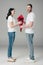 Young man gifting bouquet of red roses to pretty girlfriend on grey background