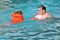 Young man and girl in lifejacket bathing in pool