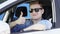 Young man gives thumb up in his car. Handsome brunette guy cool face in a car window. Blue screen chroma key background