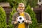 Young man with glasses in everyday clothes posing with soccer ball on green lawn