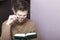 A young man with glasses reflects on an open book. Hand holding glasses for the bow. Thoughtful reading