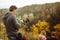 Young man going to shoot couple of tourists in love sitting on top of mountain in Autumn nature. Rear view of cameraman