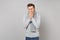 Young man in gray sweater, scarf sneezing or coughing covering mouth with hands on grey wall background