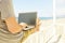 Young man in grey shirt sitting at the beach, working on laptop. Blogger, writer, coder, remote worker surfing browsing researchin