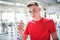 Young man in gym holding a glass of protein drink. Copy space.