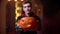 Young man in a Halloween costume of Count Dracula raises a carved pumpkin