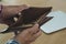 Young man hands holding brown opened empty wallet on wooden table with laptop background. He was in financial trouble after being