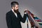 Young man with handsome serious face and beard holding many different ties in his hand on gray background studio.