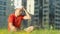 A young man in a hat resting sitting on the grass in a city park, the camera tracking