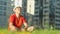 Young man in a hat resting sitting on the grass in a city park, the camera tracking