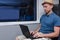 Young man in hat working behind a laptop sitting in a train chair