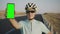 A young man in a helmet and sunglasses holds a chromakey phone vertically at arm`s length. The cyclist shows the camera