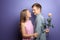 Young man hiding beautiful flower for his beloved girlfriend behind back on color background