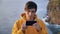 Young man hiker traveler standing on mountain and scrolling smartphone on background of cliff and ocean waves