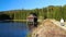 Young man hiker walk on path in nice landscape with pond, wood building and forest