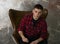 A young man in a hipster shirt sits in a beautiful chair