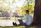 Young man with his laptop sitting in city park outdoor near lake