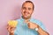 Young man holding bowl with extruded corn standing over isolated pink background very happy pointing with hand and finger