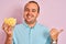 Young man holding bowl with extruded corn standing over  pink background pointing and showing with thumb up to the side