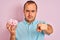 Young man holding bowl with marshmallows standing over isolated pink background pointing with finger to the camera and to you,