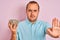 Young man holding bowl with sunflowers seeds standing over isolated pink background with open hand doing stop sign with serious