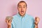 Young man holding bowl with sunflowers seeds standing over isolated pink background screaming proud and celebrating victory and