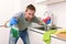 Young man holding cleaning detergent spray and sponge washing home kitchen clean angry in stress