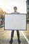 Young man holding an empty sign, board or placard while standing outside in the city street. Portrait of one happy