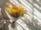 Young man holding a large bouquet of yellow mimosa flowers, against sunlit white wall with shadows of foliage. Generative AI