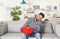 Young man holding plastic basin under water leakage from ceiling and calling plumber