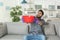 Young man holding plastic basin under water leakage from ceiling at home.