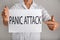 Young man holding sheet of paper with words PANIC ATTACK on light background