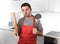 Young man holding skimmer and rolling pin wearing apron at home