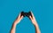Young man holding videogame joystick on blue background, closeup of hands