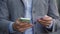 Young man holding visit card and smartphone, typing outdoors. Slow motion