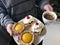 A young man holds a cup of coffee and a plate of cakes.