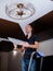 A young man is installing a plafond on a ceiling chandelier in the hall, standing on a stepladder