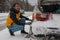 Young man is installing snow chains on a vintage car on snow and icy roads. Man struggling to get the car snow chains onto winter