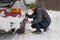 Young man is installing snow chains on a vintage car on snow and icy roads. Man struggling to get the car snow chains onto winter
