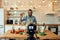 Young man, Italian cook in apron waving at camera, greeting audience, filming himself for culinary blog while preparing