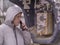 A young man in a jacket with a hood is talking to an old payphone on the street