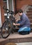 Young man in jeans and shirt repairing bicycle at house backyard