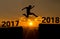 A young man jump between 2017 and 2018 years over the sun and through on the gap of hill silhouette evening colorful sky.